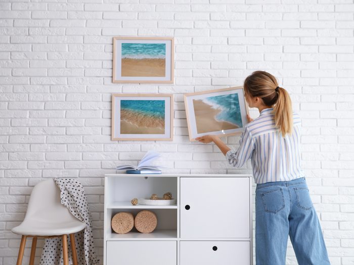 Decorator,hanging,picture,on,white,brick,wall,in,room.,interior