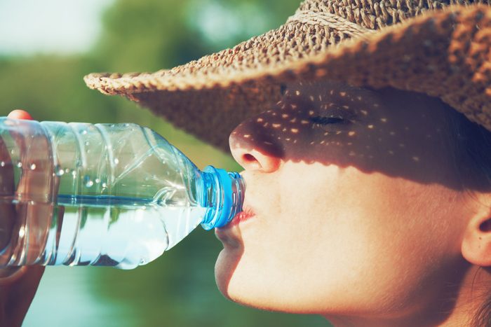 Gros plan sur une femme portant un chapeau de paille qui boit une bouteille d'eau.