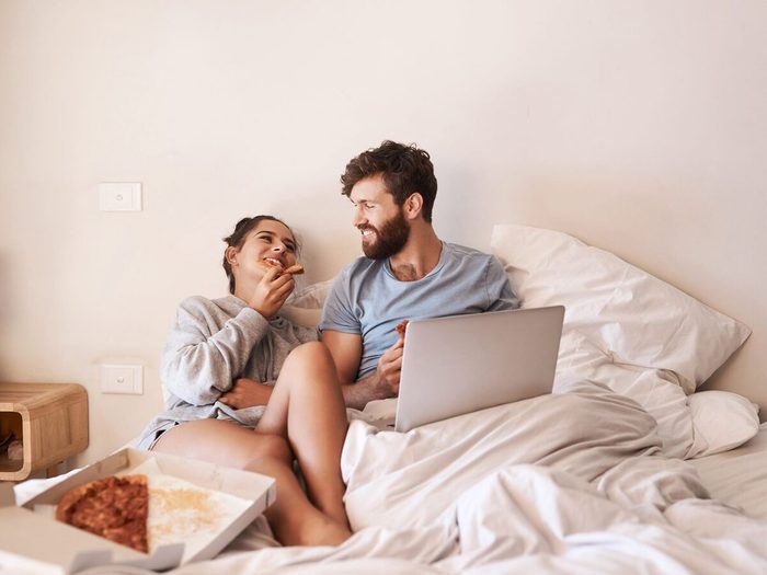 Un couple heureus mange une pizza dans leur lit.