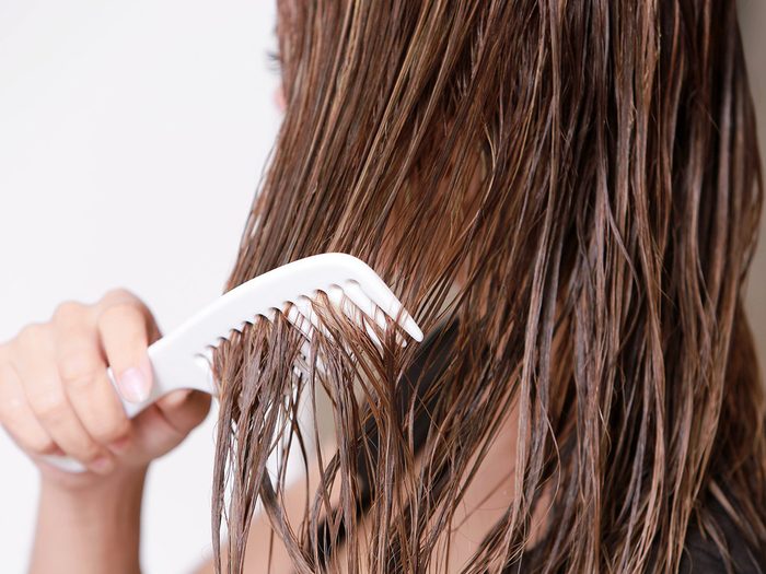 Une jeune fille passe une brosse sur ses cheveux mouillés et abimés.