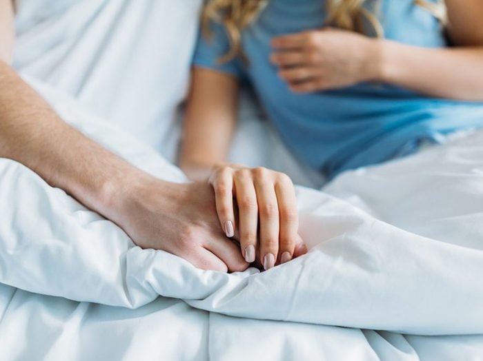 Sexe: un couple se tient les mains au lit.