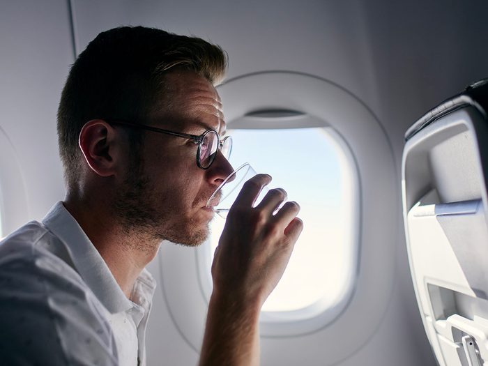 Homme buvant un verre d'eau dans un avion près d'un hublot.