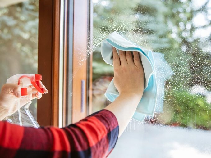 Woman Is Wiping The Cleaning Liquid From The Window With Garden In The Background.