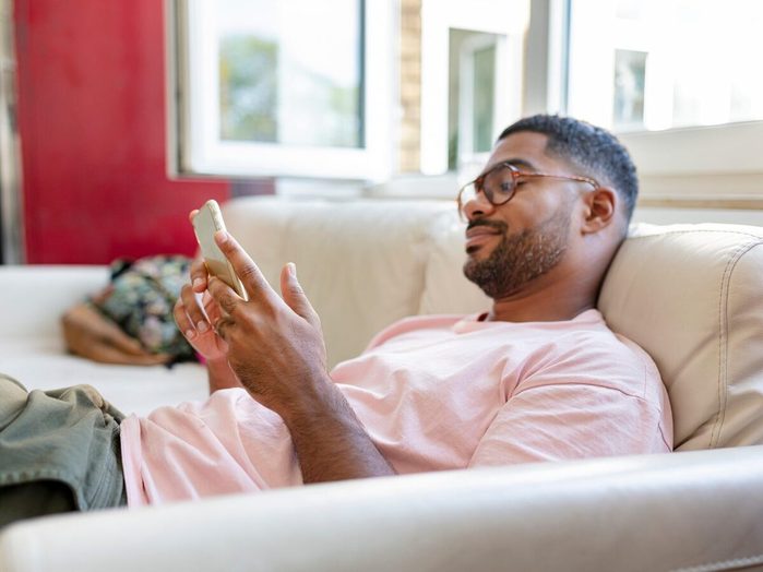 Relaxed Man Sitting On Sofa Using Cell Phone