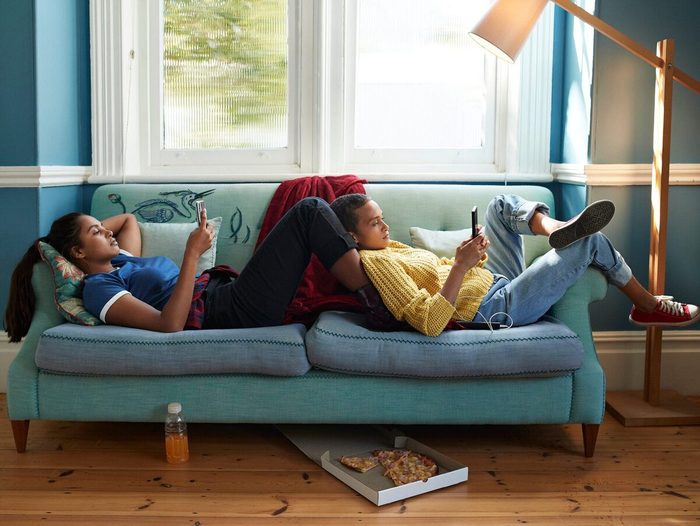 Women Using Phones While Relaxing On Sofa