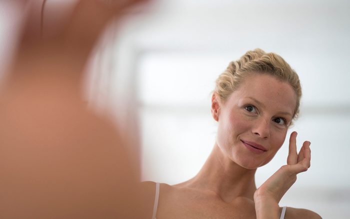 Femme devant le miroir qui met de la crème sur son visage.