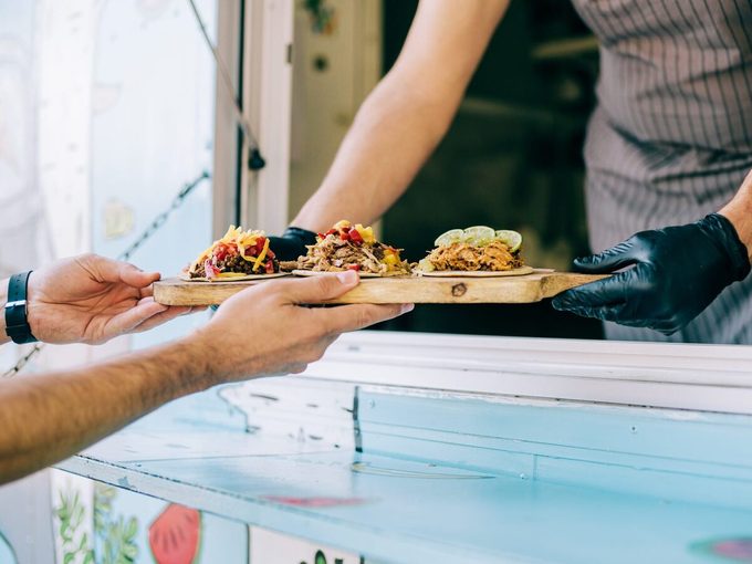 Food Truck Owner Serving Tacos To Male Customer.