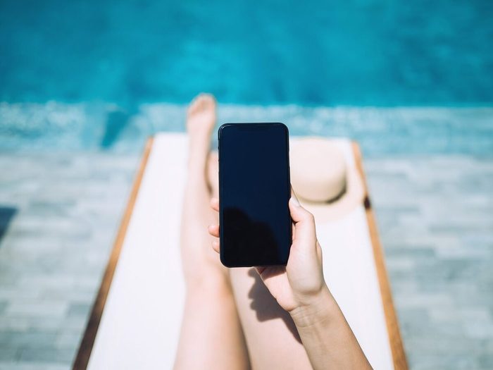 Low Section Of Young Woman Using Smartphone While Enjoying The Sun On Lounge Chair By The Pool Side