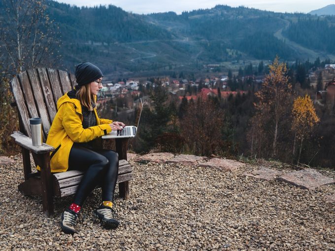 Woman,wearing,glasses,and,yellow,jacket,working,on,laptop,outdoors