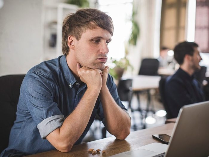 Tensed Businessman Looking At Laptop While Sitting At Desk In Creative Office