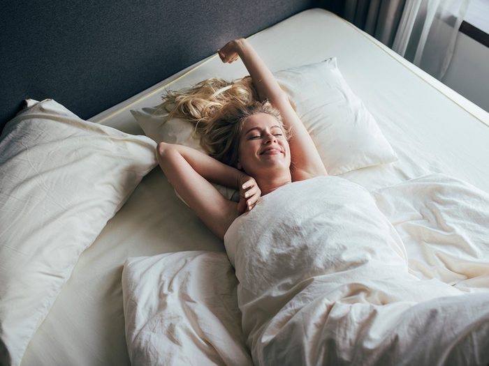 Dormi nu: une femme s'étire dans son lit