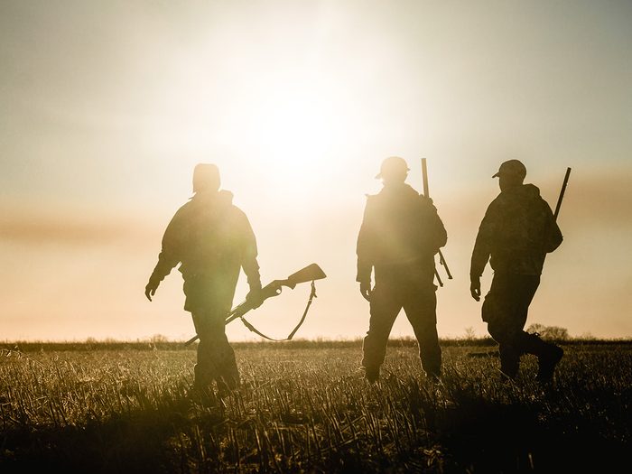 Trois chasseurs marchent pendant le coucher du soleil.