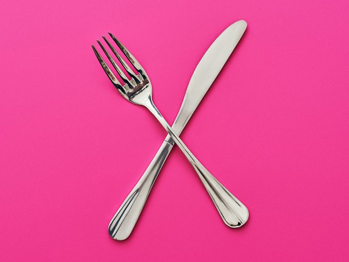 Une fourchette et un couteau sur un fond rose.