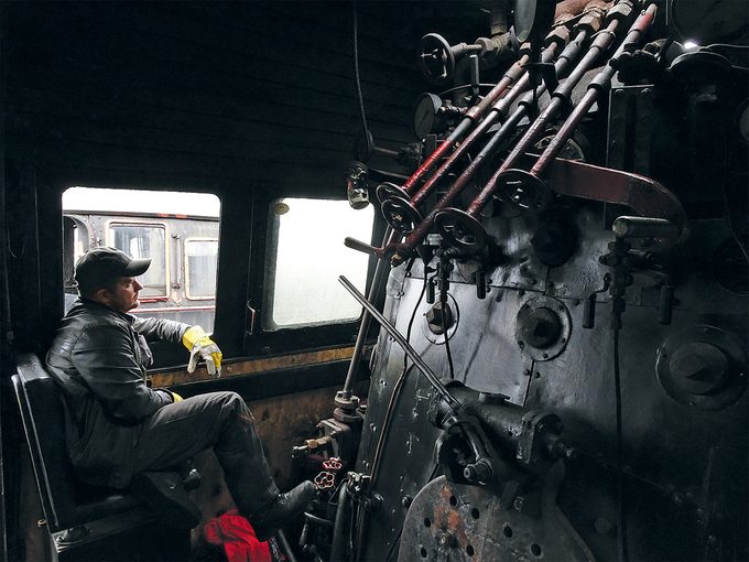 Train à vapeur: Marcin, le chauffeur, dans la cabine de la locomotive, entouré d’un éventail de leviers et de poignées.